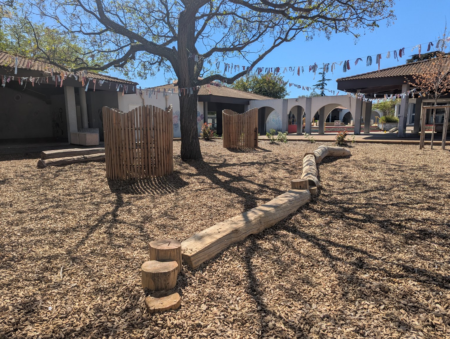 Référence photographique : une cour d'école avec des arbres, des copeaux et des éléments en bois.