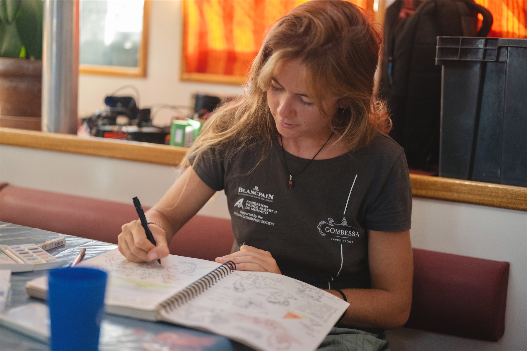 Aline dessinant dans un carnet à la table de la cabine.