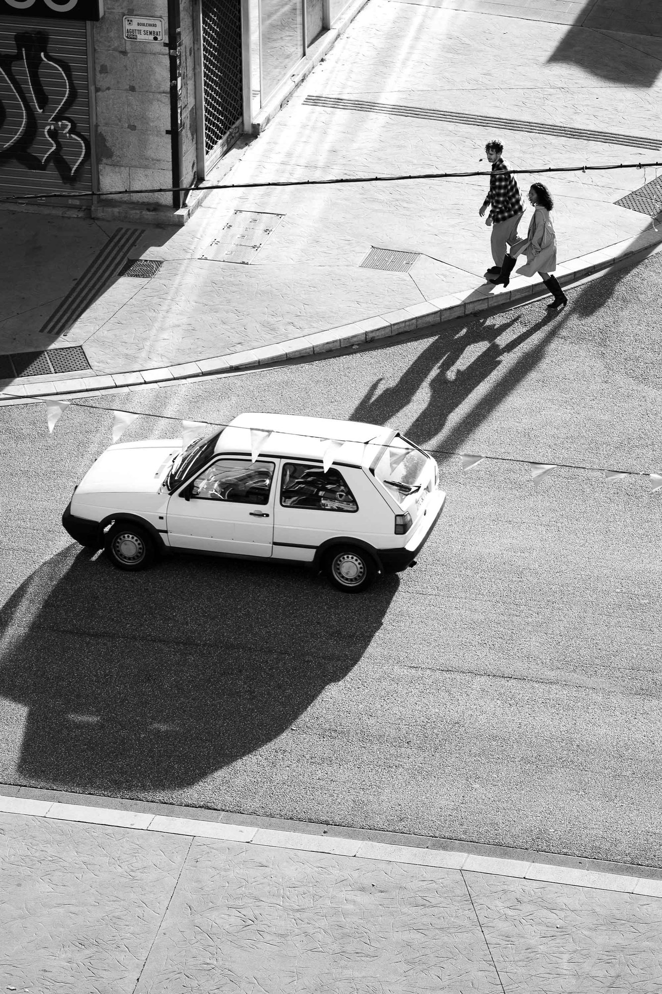 Passants et voiture dans une rue de Grenoble, en noir et blanc.